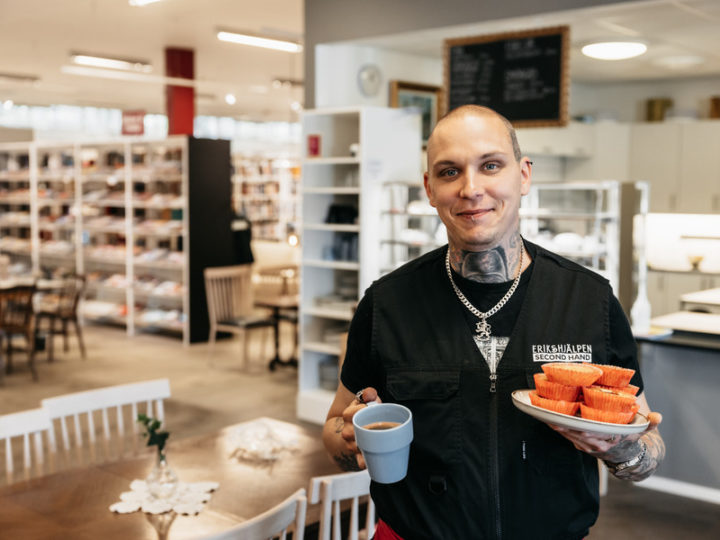 En glad medarbetare i Eriks kafé håller en kaffe och muffins