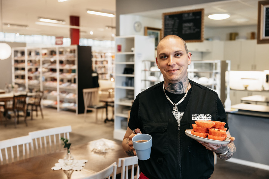 En glad medarbetare i Eriks kafé håller en kaffe och muffins