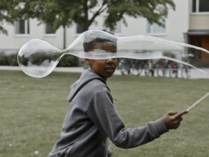 En pojke springer med en jättestor såpbubbla genom ett bostadsområde