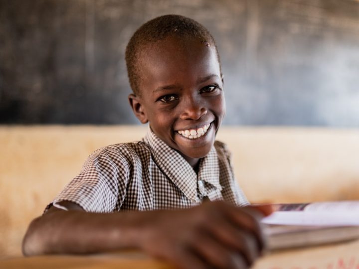 Ett barn sitter vid en skolbänk och ler brett.
