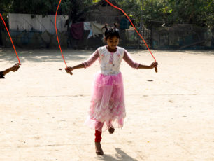 En flicka i rosa klänning hoppar hopprep på en solig skolgård i Bangladesh.