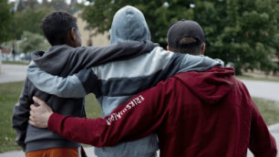 Tre killar bakifrån som håller varandra om ryggen där personen längst ut till höger har en Erikshjälpen-hoodie på sig.