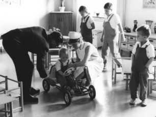 Erik Nilsson står vid ett barn i en lekbil i sjukhusets lekrum