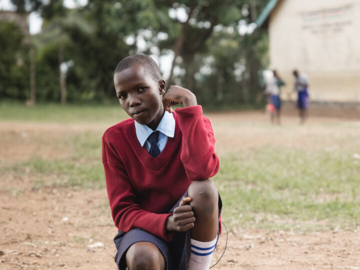 En elev iklädd skoluniform sitter på huk utanför sin skola.