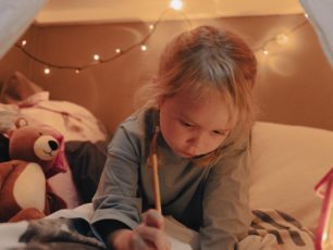 En flicka sitter i sängen och skriver en önskelista till jul.