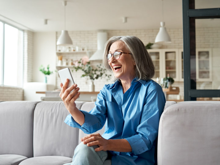En glad äldre kvinna tittar på sin mobil.