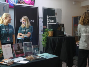 Två leende kvinnor som jobbar som värvare för Erikshjälpen står i en monter på ett evenemang och pratar.