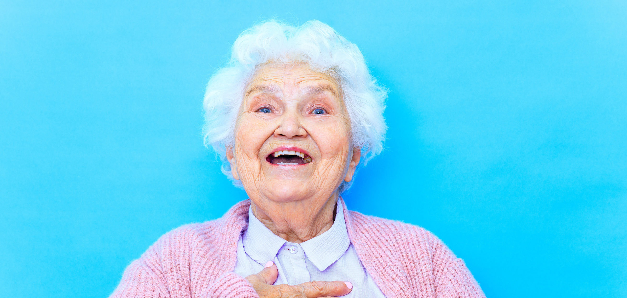 Äldre mormorsliknande kvinna i rosa kofta som skrattar och håller sig för bröstet.