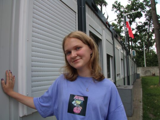 Viktoria står med handen lutad mot väggen och ler hoppfullt.