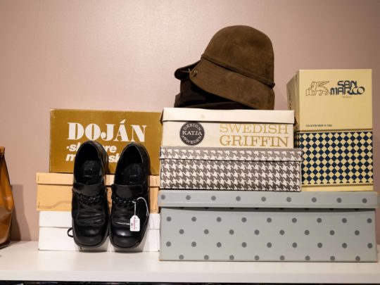 Skokartonger, en hatt, en väska och ett par skor står uppställda på en hylla i en second hand-butik.