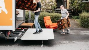 En soffa bärs in i en lastbil framför ett hus. En fåtölj och kuddar är på tur.