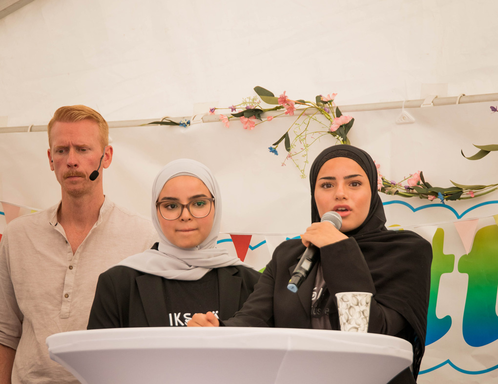 Två tjejer från Erikshjälpen Framtidverkstad står vid ett podium och pratar i en mikrofon.