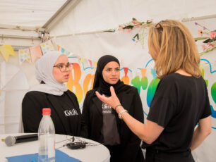 Två tonårstjejer pratar engagerat med en vuxen kvinna. Kvinnan gestikulerar med sina händer. Tjejerna lyssnar intresserat.