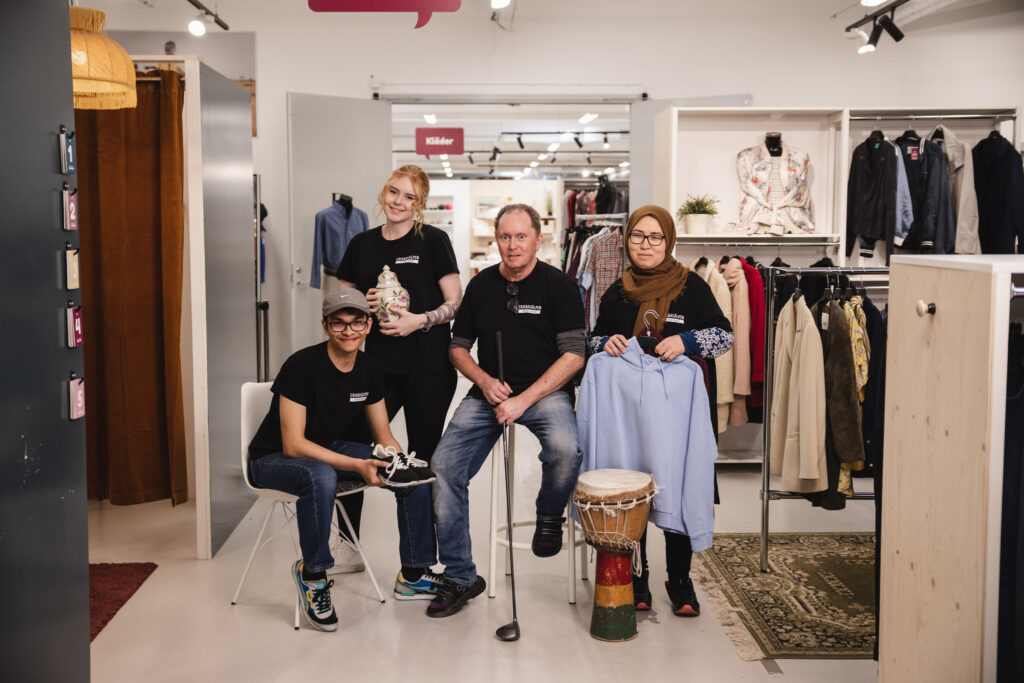 Fyra volontärer i en av Erikshjälpen Second Hands butiker. En sitter på en stoll, en på en pall, en håller i en skjorta och den fjärde håller i en vas.