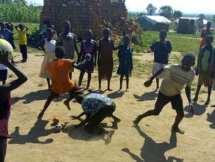 Barn leker med bollar på en grusplan i Afrika. Solen skiner.