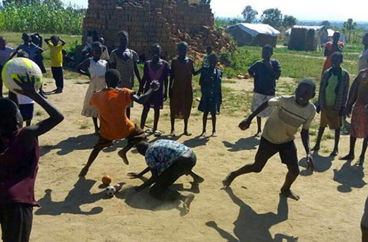 Barn leker med bollar på en grusplan i Afrika. Solen skiner.