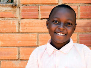 Ezekiel är 11 år och bor i Uganda. Han står framför en väg gjord av tegel, iklädd en vit skjorta.