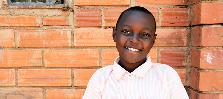 Ezekiel är 11 år och bor i Uganda. Han står framför en väg gjord av tegel, iklädd en vit skjorta.