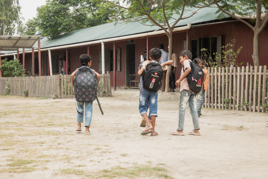 Tre killar på en skolgård i Bangladesh. De bär ryggsäckar och är påväg mot klassrummet.