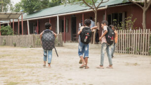 Tre killar på en skolgård i Bangladesh. De bär ryggsäckar och är påväg mot klassrummet.