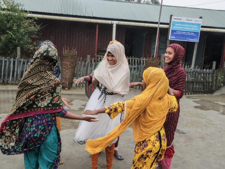 Barn håller varandra i händerna och dansar i en cirkel på en skolgård i Bangladesh.