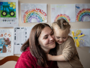 En mamma kramar sitt barn. De har kinderna mot varandra. I Bakgrunden syns en vägg fylld av teckningar.