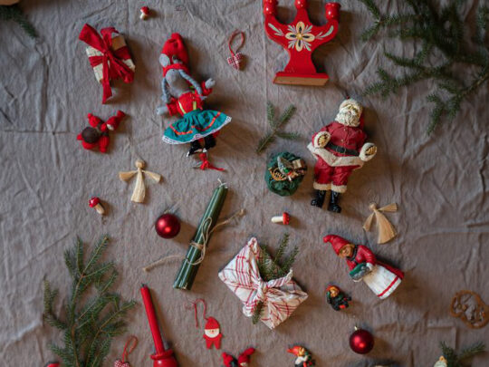 Ett bord med en grå duk fylld av saker som är starkt förknippade med julen som exempelvis tomtar, grankvistar och julgranskulor.