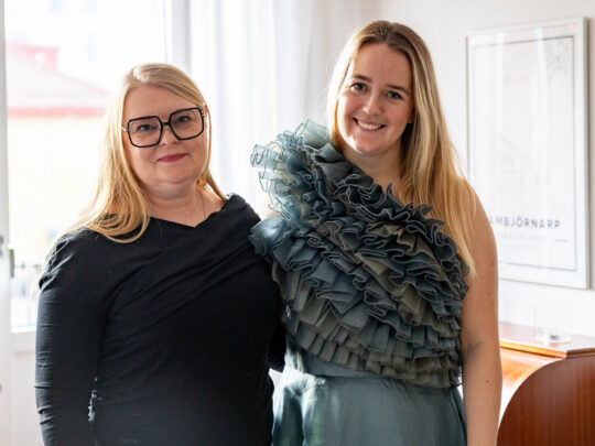 Designer Sofia Corneskog with the winner of the dress raffle, Miranda. They are standing in Miranda's living room. Miranda is wearing the dress.