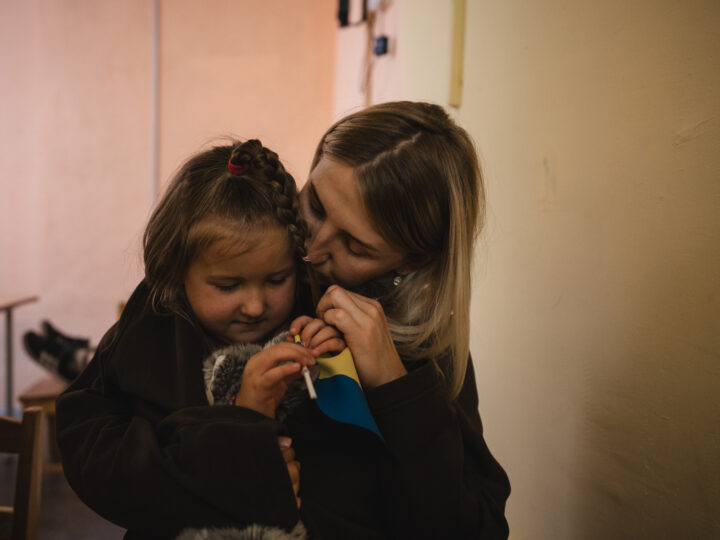 En mamma som kramar om sin dotter som hållerr i en liten Ukrainaflagga.