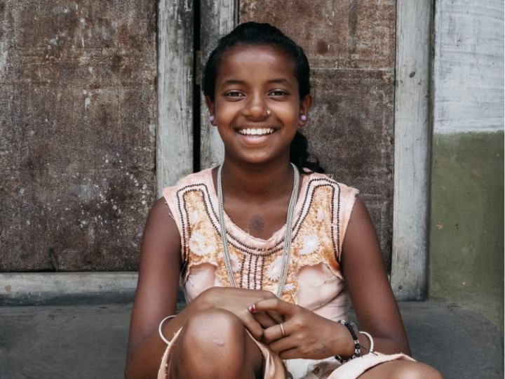 Flicka sitter i en stentrappa i Indien och ler mot kameran.