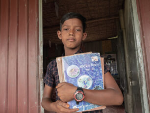 Shamin, 12 år står med skolböcker i famnen, i dörren till en flyttbar skola.