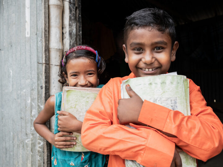 Två glada barn står med skolböcker i famnen.