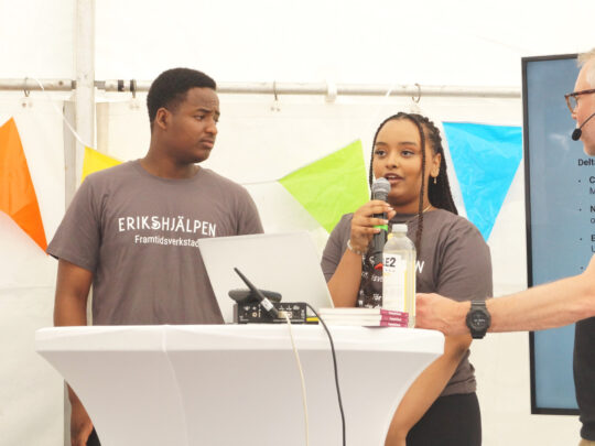 Två ungdomar står i ett tält i Almedalen tillsammans med Erikshjälpens generalsekreterare Mattias Ingeson. En av ungdomarna talar i en mikrofon.