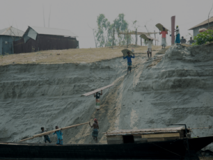 Män som flyttar på delar från en nedmonterad skola ner från en sandbank till en båt.