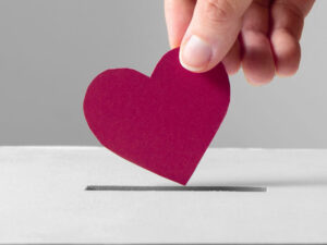 Hand lägger i ett vinrött pappershjärta i en insamlingsbox.