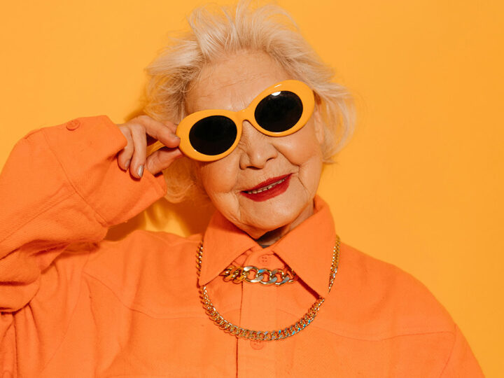 En dam klädd i orange skjorta och orangea solglasögon står framför en orange vägg.