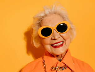 En dam klädd i orange skjorta och orangea solglasögon står framför en orange vägg.