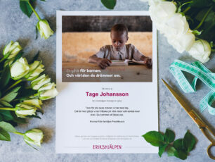 Gåvobevis till Minnesgåva från Erikshjälpen. Vita blommor, en guldig sax och ett tyg snöre ligger runt gåvobeviset.