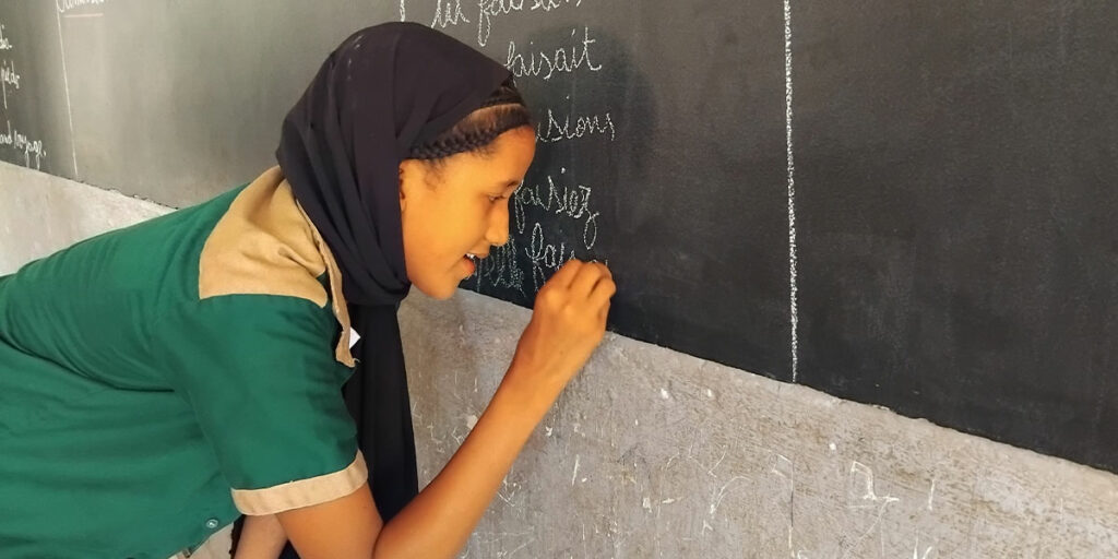 Fatoumata skriver på griffeltavlan i skolan.