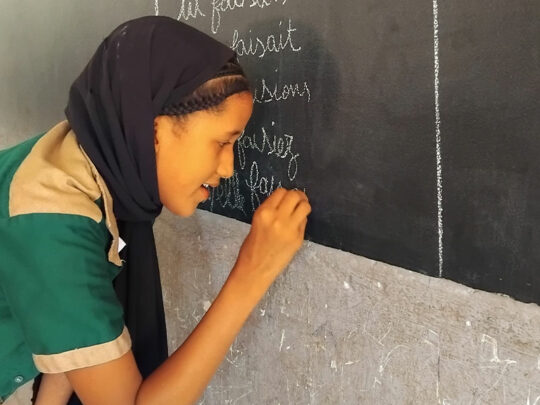 Fatoumata skriver på griffeltavlan i skolan.