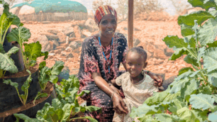 En mamma och ett barn poserar bland frodande växtlighet familjen trädgård med kägelodling i Kenya.