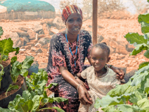 En mamma och ett barn poserar bland frodande växtlighet familjen trädgård med kägelodling i Kenya.