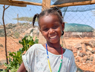 A child smiling in a fenced homegarden.