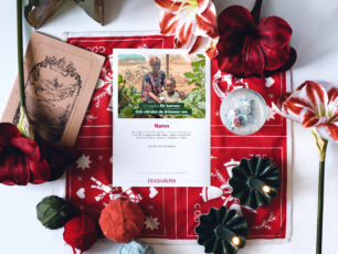 Ett gåvobevis från Erikshjälpen ligger på en röd julig duk, tillsammans med en snöglob, julamaryllis, två gröna ljusstakar med levande ljus och andra juliga saker.