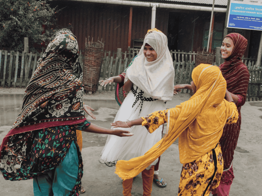 Barn håller varandra i händerna och dansar i en cirkel på en skolgård i Bangladesh.