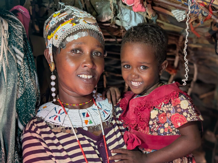 En glad mamma håller sin dotter i famnen i den egna kiosken i Kenya.