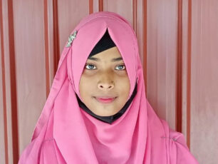 Hiramoni står mot en skolvägg.