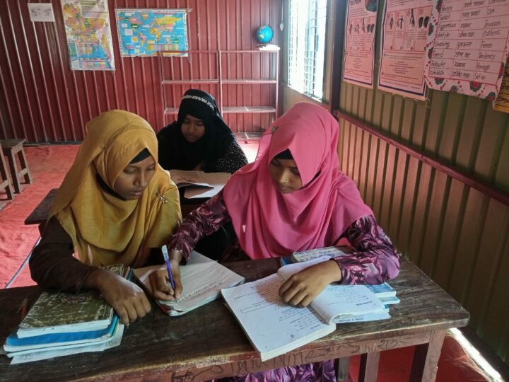 Hiramoni skriver i en klasskamrats skolbok. De sitter i skolbänkarna i en flyttbar skola i Bangladesh.