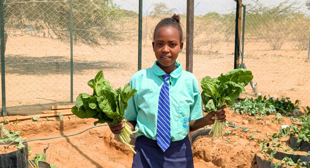 Sabina holding bundles of spinach from their school farm