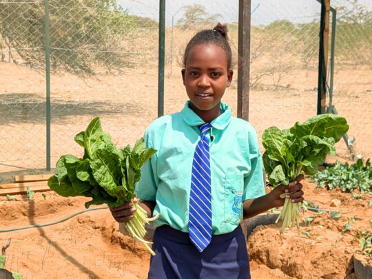 Sabina holding bundles of spinach from their school farm